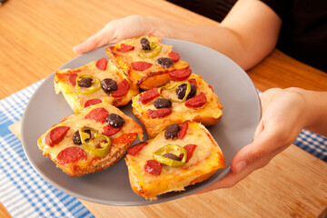 Caucasian person with fair skin holding tasty pizza pieces in gray plate on blue napkin and bamboo cutting board,