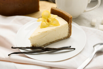 Plate of sweet cheesecake with vanilla flower and sticks on white background