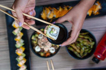 sumergiendo un sushi en soja con palillos y de fondo mas comida
