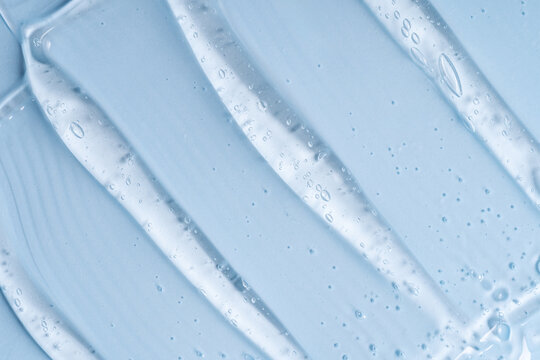 Close-up shot of blue liquid cosmetic gel or serum makeup swatches with a glossy, shiny texture on a smooth blue background