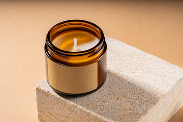 Mock-up of aroma soy candle in amber glass jar on natural stone pedestal. Scented cozy atmosphere for relax and spa on brown background, mockup