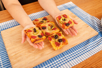 Caucasian white person holding pizza pieces on bamboo cutting board on blue napkin