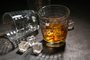 Composition with glass of cold rum, empty glass and ice cubes on grey grunge background, closeup