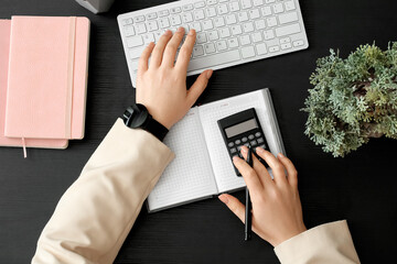 Businesswoman working with computer and calculator on dark table, top view