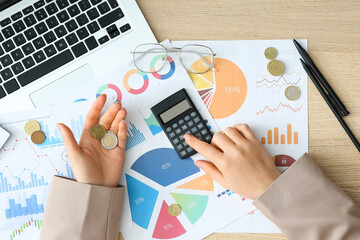 Businesswoman with coins using calculator on wooden table, top view. Financial Wellness Month