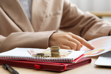 Money on notebooks against businesswoman with diagrams at table, closeup. Financial Wellness Month