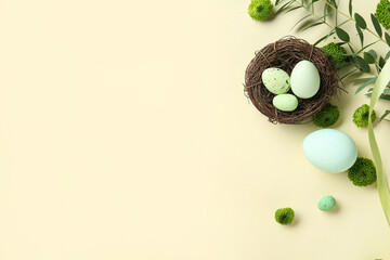 Easter eggs, decorative nest, green twigs and flowers on beige background