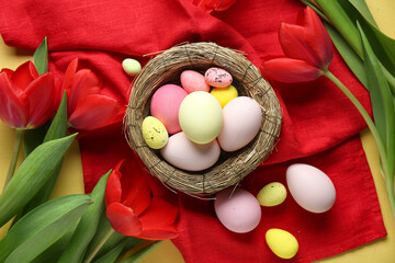 Easter eggs, decorative nest, napkin and tulip flowers on yellow background