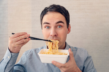 young, handsome, cheerful man is eating delicious instant noodles with chopsticks