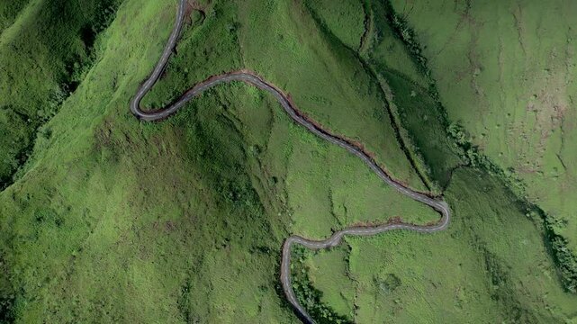 Drone footage of a winding mountain road cutting through lush green hills. A perfect shot for travel and nature