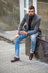 Coffee break. Everyday style routine. Bearded man having coffee in city street. Handsome man on street holding cup of coffee. Business lifestyle, break. Man drinking morning coffee. Male model