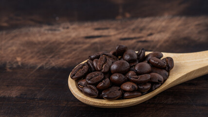 Wooden spoon filled with roasted coffee beans on a rustic wooden background. Aromatic and fresh coffee concept.