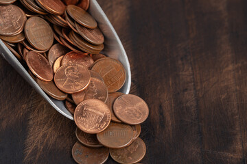 Metal scoop filled with U.S. pennies spilling onto a rustic wooden surface. Concept of savings, financial planning, and small investments.