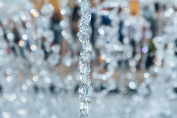 A splashing fountain in the center of the city with a selective focus and a blurry background of people walking. A running fountain with splashes and drops of water.Frozen water droplets in the air