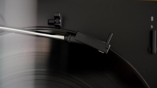 Automatic tonearm in vinyl record player starting to play. Listening to classic analog music with vintage sound. Close-up with black vinyl