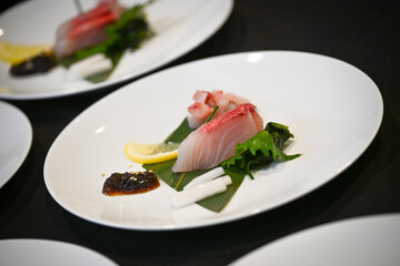 Sliced fish is artfully placed on a bed of greens, garnished with fresh lemon and a rich sauce, showcasing the elegance of Japanese culinary presentation.