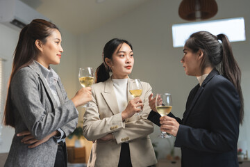 Three professional women converse while holding glasses of white wine. They appear to be networking...