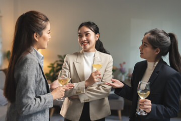 Three professional women engage in a lively business networking discussion while holding glasses of white wine, showcasing confidence and camaraderie in a modern office setting