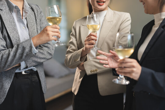 Group of business professionals enjoying white wine together, engaging in conversation. They are dressed in formal attire, suggesting a networking or social event in a modern setting