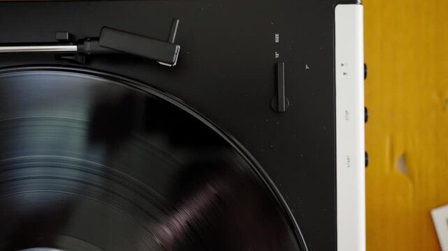 Automatic tonearm in vinyl record player starting to play. Listening to classic analog music with vintage sound. Close-up with black vinyl
