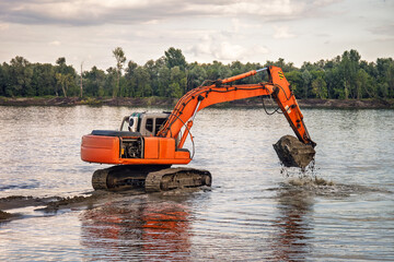 excavator cleans river bed from silt and threaten. Construction of a bridge or dam in case of...