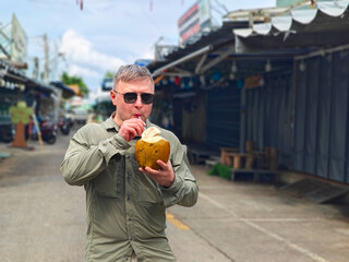 A man in sunglasses and a khaki shirt enjoys fresh coconut water