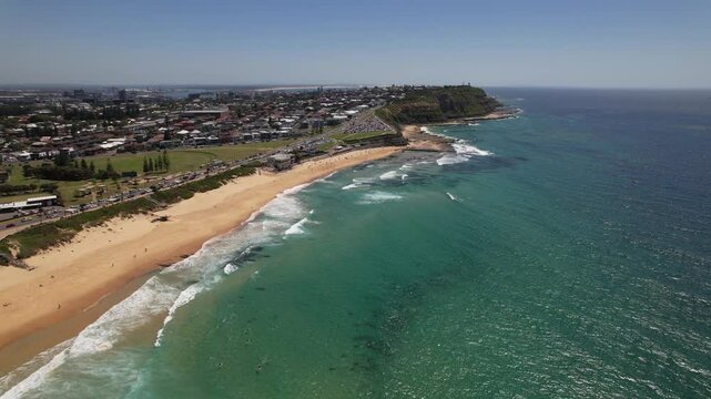 Surfers And Splashing Waves At Merewether Beach On Sunny Day In Newcastle, NSW, Australia. aerial descend