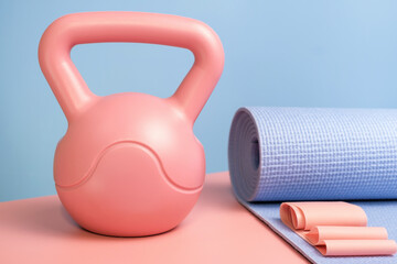 Kettlebell and sports mat on a pink and blue background front view close-up.