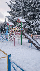 Children's playground covered with snow. Empty swings and slides.