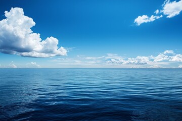 Obraz premium A vast, calm sea under the blue sky, with a white cloud in sky. The water is deep and serene, reflecting the clear sky above it. 
