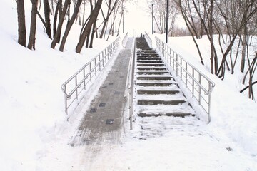 Snow-covered stairs and ramp with metal railings, providing accessibility for people with disabilities. Inclusive design, overcoming obstacles in public park. Winter landscape, outdoor passage concept