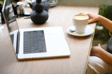 A woman works on her laptop in a café, sipping coffee. The cozy atmosphere and soft lighting create a productive yet relaxed environment for her to focus and enjoy her beverage.