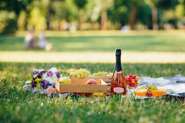 Summer picnic in nature: fresh fruits, chilled champagne, a cozy blanket on a green lawn. Warm sunlight, a light breeze and the atmosphere of the morning