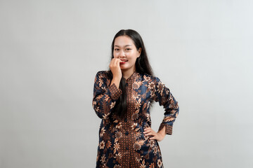 A young woman in a traditional Indonesian batik outfit, playfully biting her finger with a thoughtful expression. Her vibrant attire and pose reflect cultural pride and a lighthearted mood.