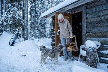 Woman in winter clothes and her dog carrying firewood outside