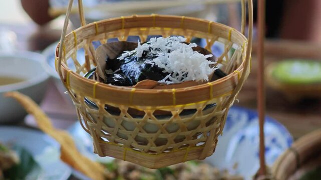 Black charcoal pandanus pudding with coconut in small basket.