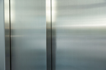 A silver metal door with a shiny, reflective surface elevator door background and texture. © Rattanachat