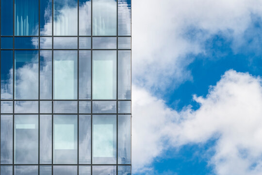 Modern glass facade reflecting a bright blue sky with scattered clouds, emphasizing symmetry and geometric patterns in contemporary architecture.