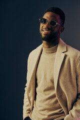 Fototapeta premium Stylish African American man in a beige coat and sweater smiling, showcasing modern fashion against a colorful studio background Seasonal autumn style portrait