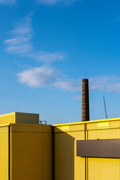 Industrial facility with striking yellow walls and a smokestack, emphasizing urban contrast and architectural texture.