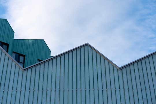 Minimalist industrial facade in light blue with distinct roof angles, presenting a clean architectural aesthetic.