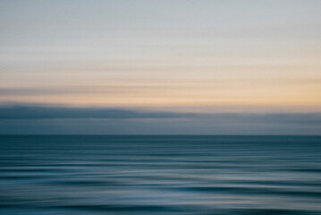 The image captures a tranquil moment in the ocean, with a clear blue sky in the background. The water appears calm and still, with no visible waves or ripples. The sky is a mix of light blue and white
