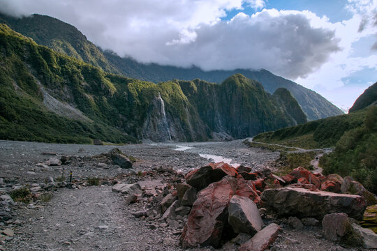 Franz Josef Glacier Walk rocky terrain along the glacial valley with rugged mountains in the background under a cloudy sky