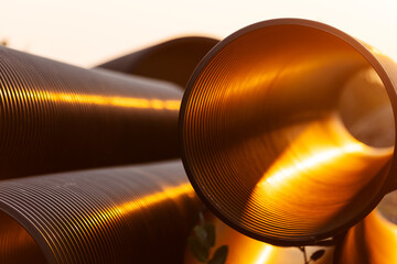 large water pipes stacked at a construction site, with sunlight illuminating the inner surface of...