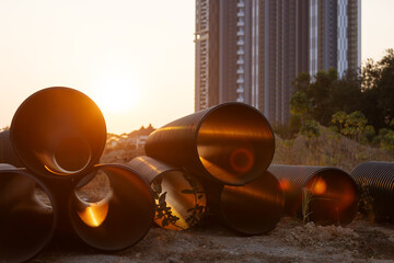 a stack of large pipes arranged at a construction site, with the setting sun casting light on them....