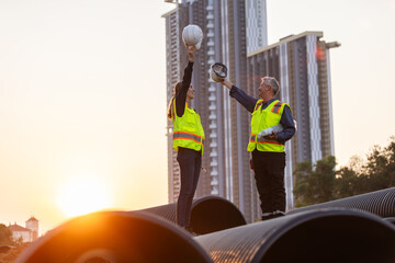 Two engineers stand on large water pipes at a construction site, celebrating the completion of their work.