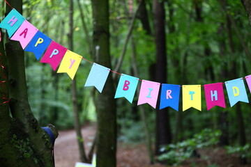 incomplete Happy Birthday inscription on colorful flags in a green forest, Happy Birthday in the...