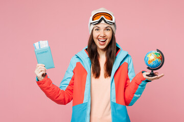 Traveler woman wear blue padded jacket ski goggles mask hold passport ticket globe isolated on plain pink background. Tourist travel abroad in free time rest getaway. Air flight trip journey concept. © ViDi Studio