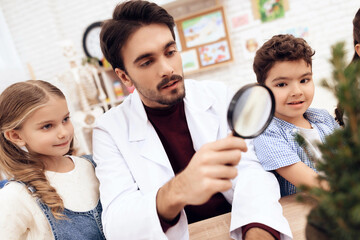 Children together with the teacher look through a magnifying glass on a plant