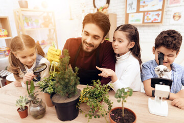 Children together with the teacher look through a magnifying glass on a plant.